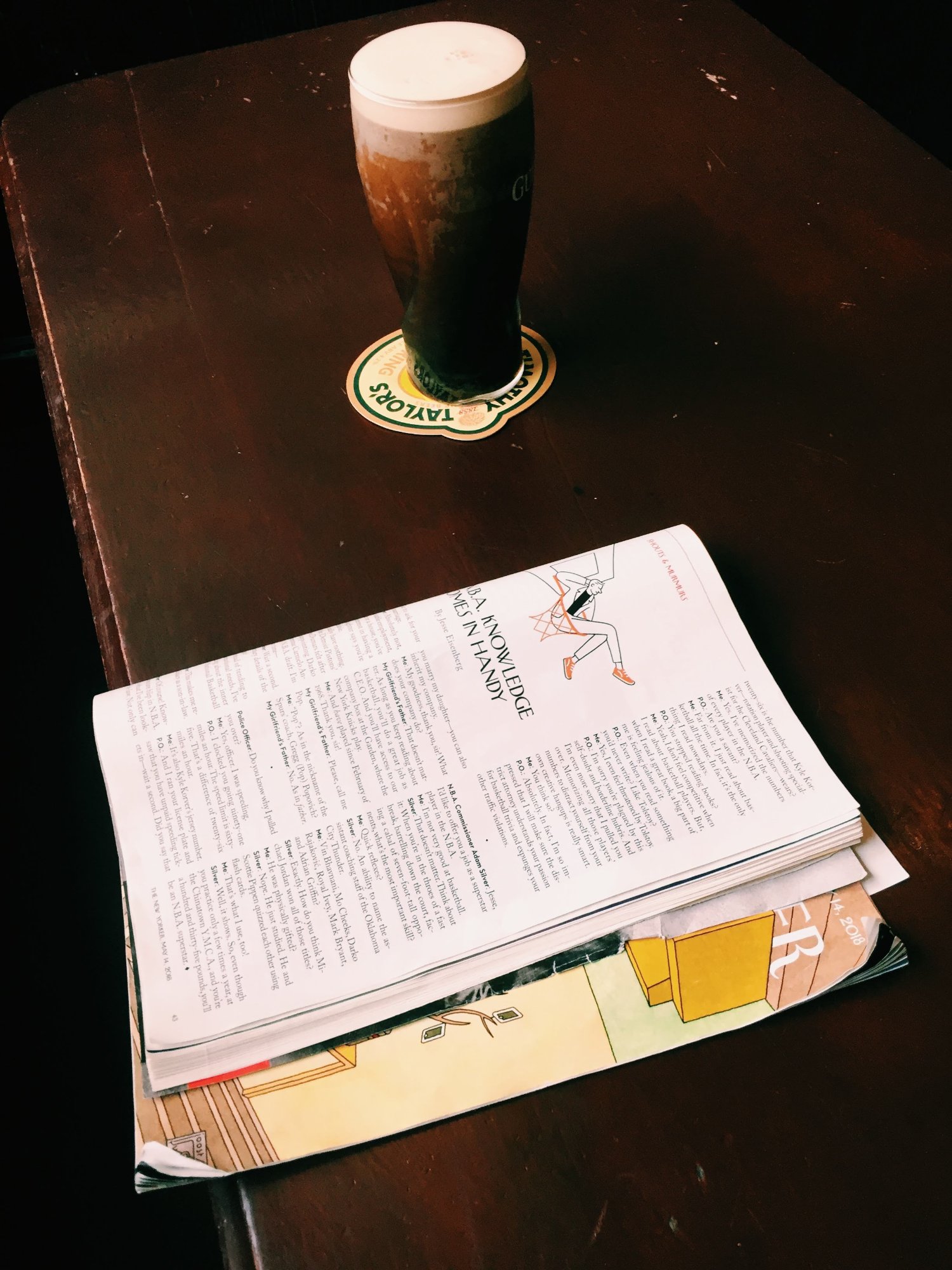 Pint of Guinness with New Yorker magazine on dark wood table