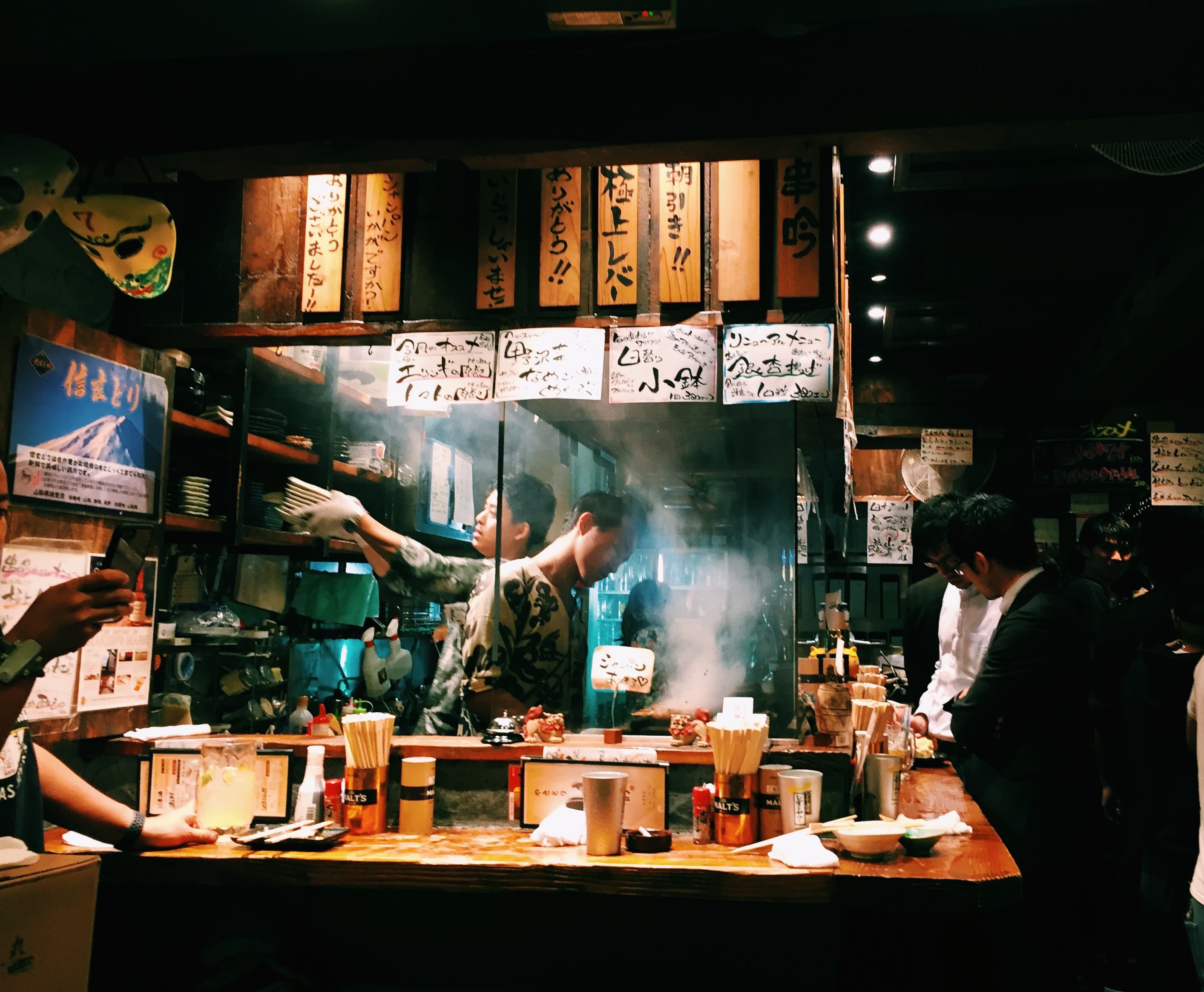 Kushigin kitchen — tattooed chef, smoke rising off the grill, packed counter