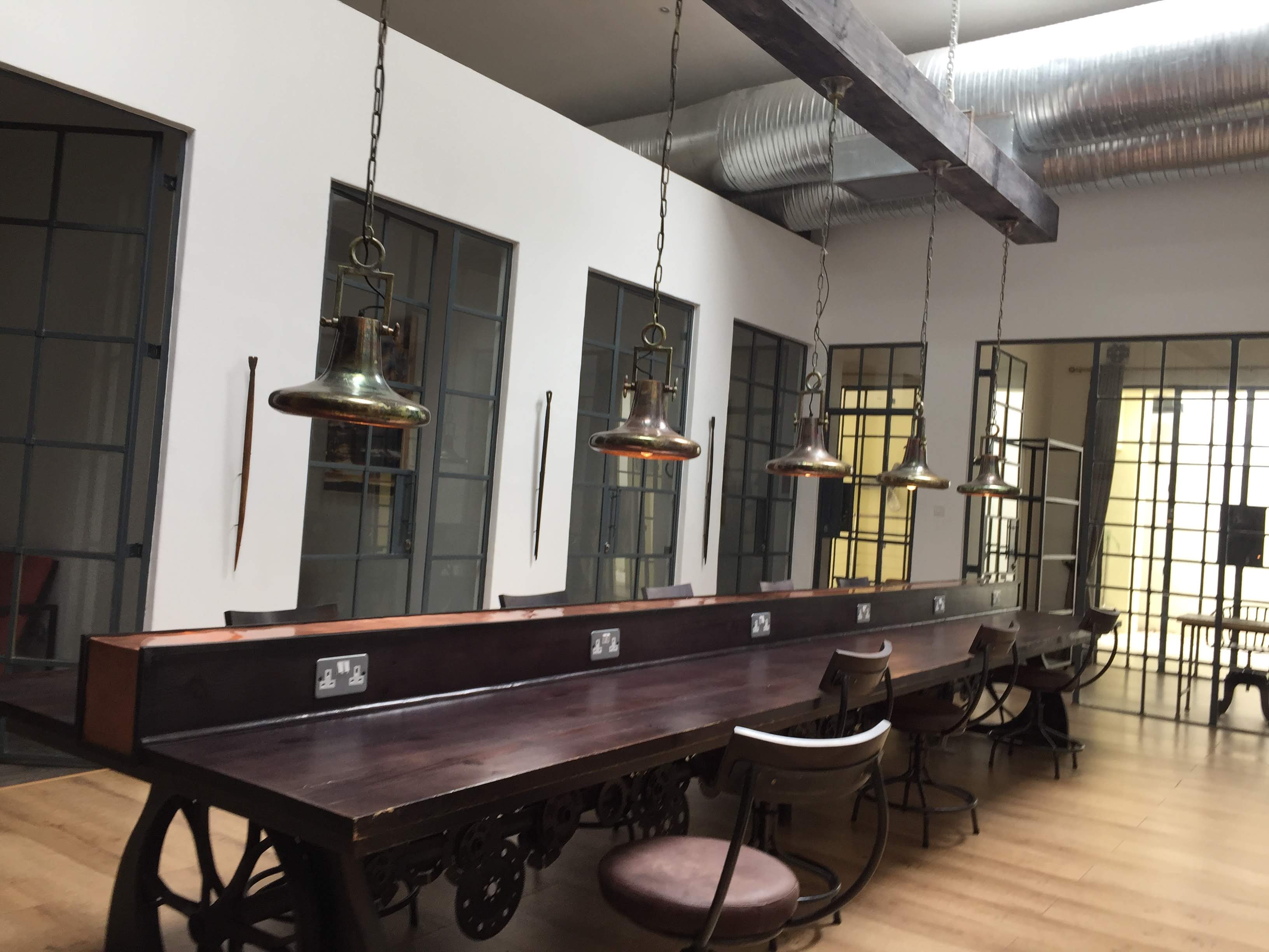 Latitude 15 co-working space — long dark wood communal table, brass industrial pendant lights, steel-framed windows