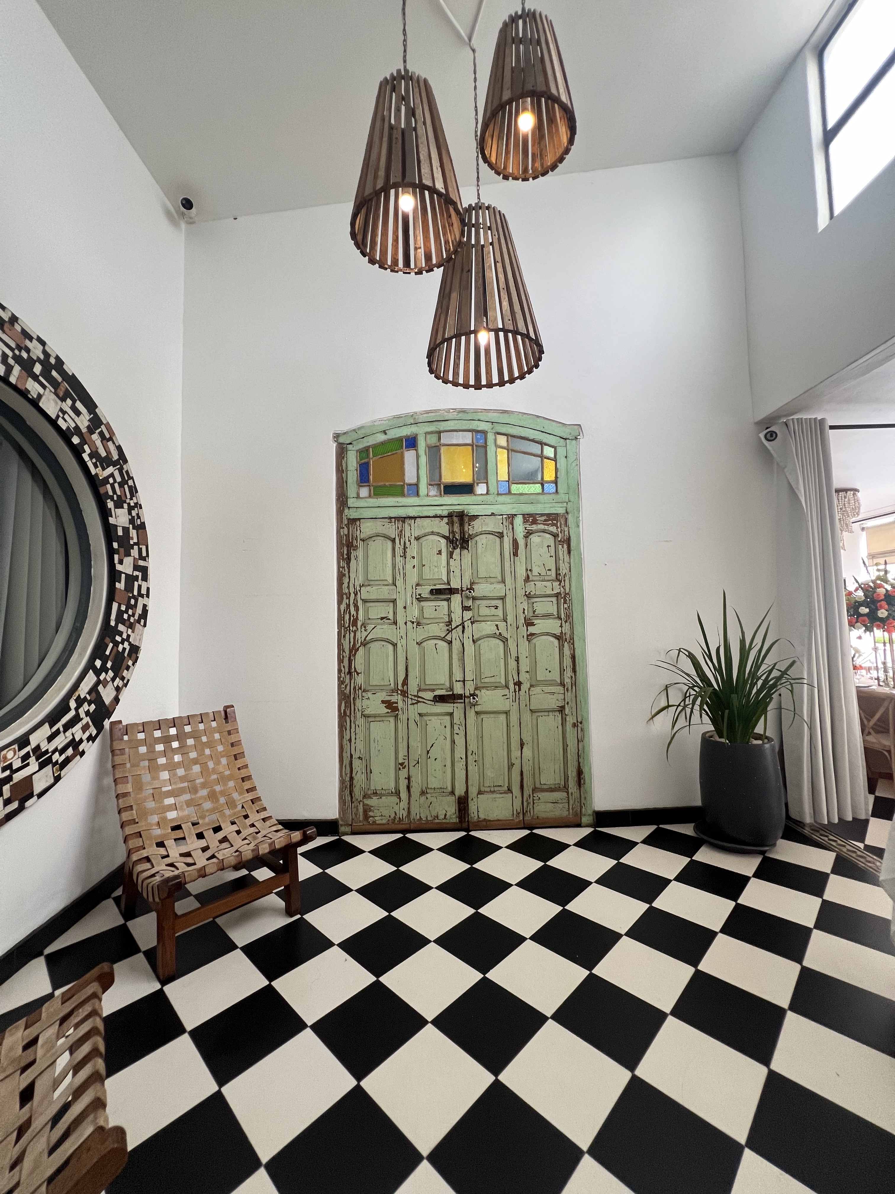 Vintage green door with stained glass transom, checkerboard floor and handcrafted wooden pendants — Latitude 15 lobby