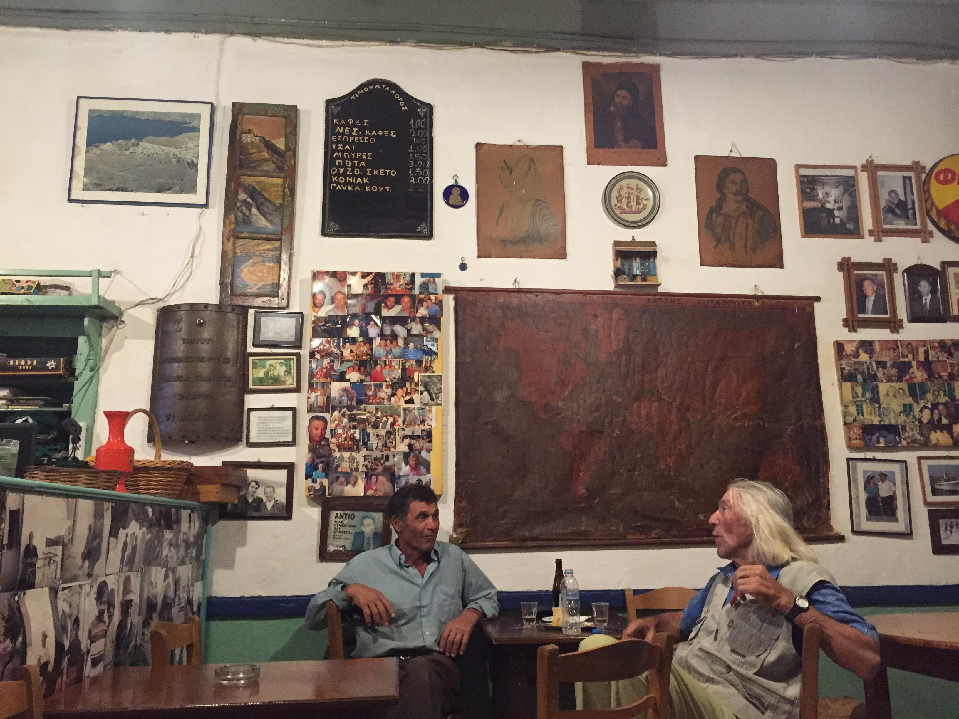 Old kafeneio interior in Astypalea, locals sitting, walls covered in photos and icons
