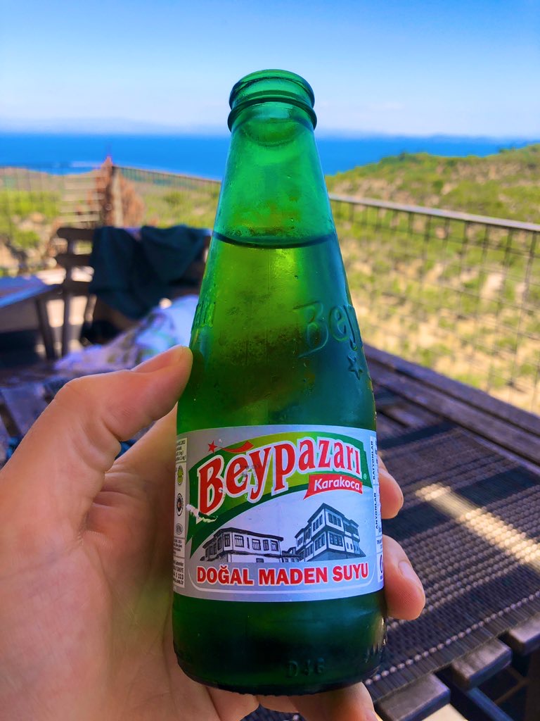 A green glass bottle of Beypazarı Karakoca sparkling mineral water held up against the Aegean coastline in Turkey