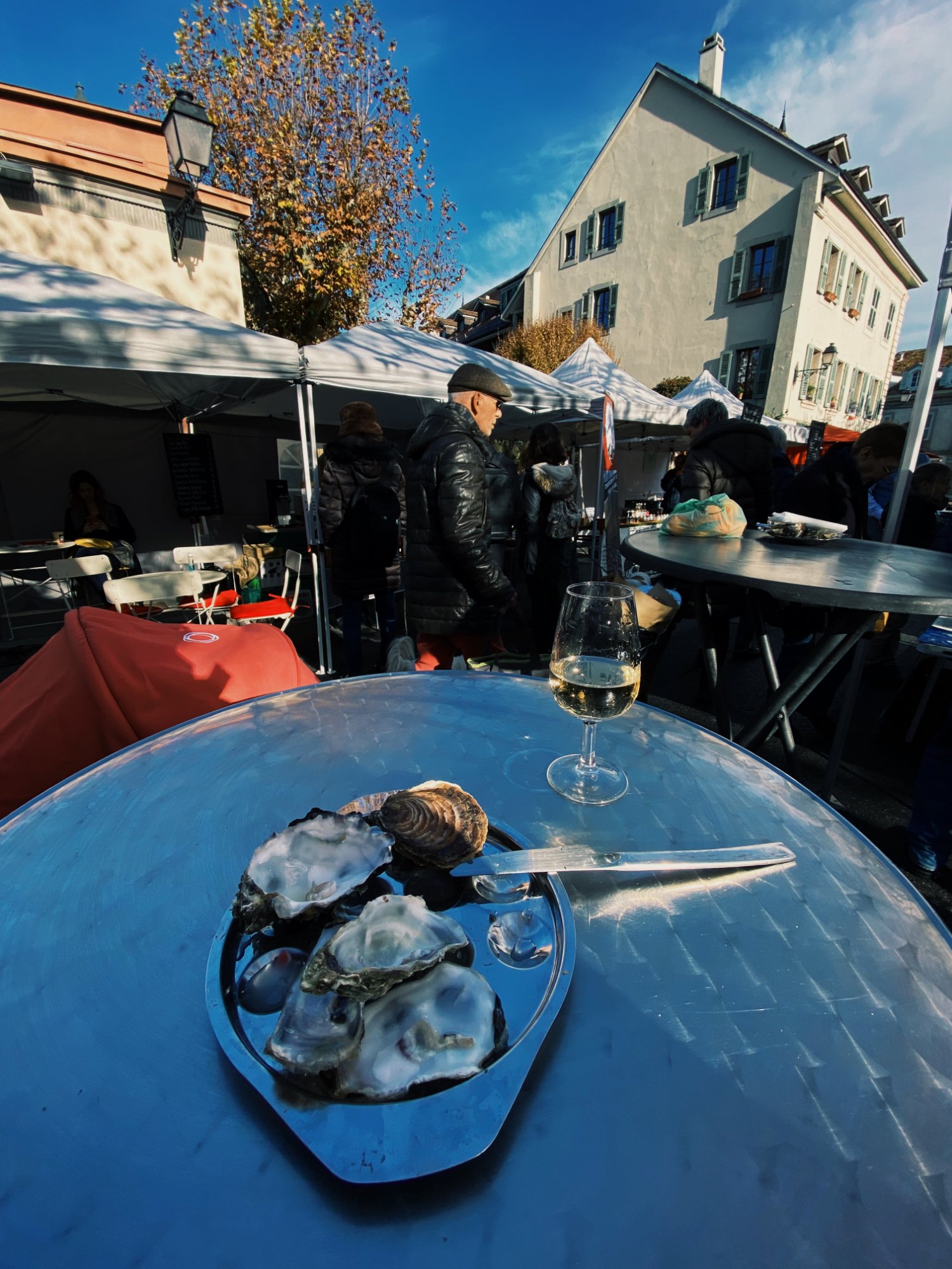 Oysters and a glass of white wine on a blue barrel table at the Carouge market