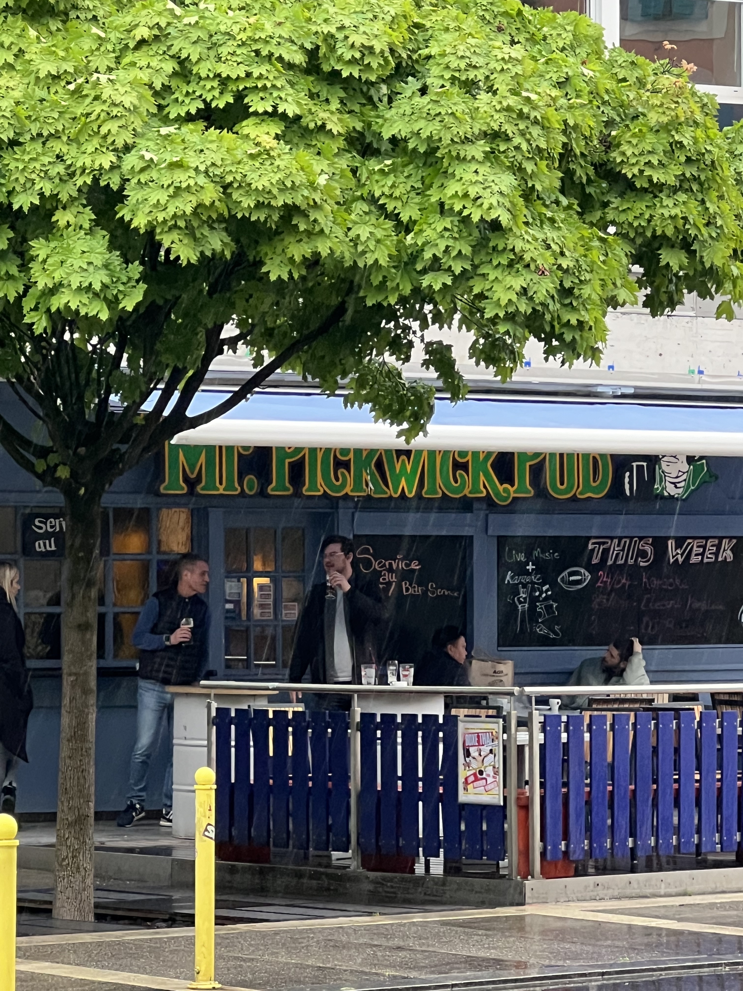 Mr. Pickwick Pub exterior in Geneva, blue facade with green and yellow lettering, terrace under a tree