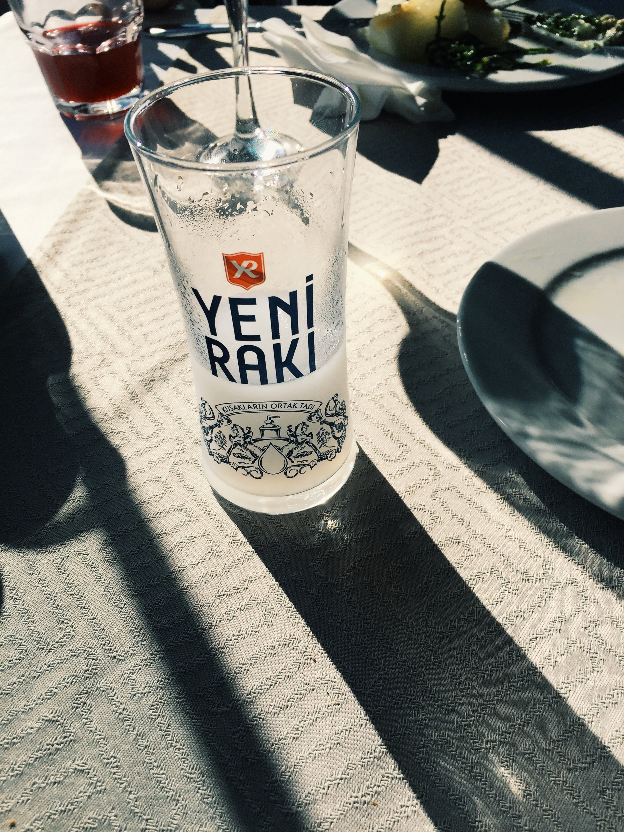 A glass of Yeni Raki on a sunlit table at Filinta, with mezze in the background