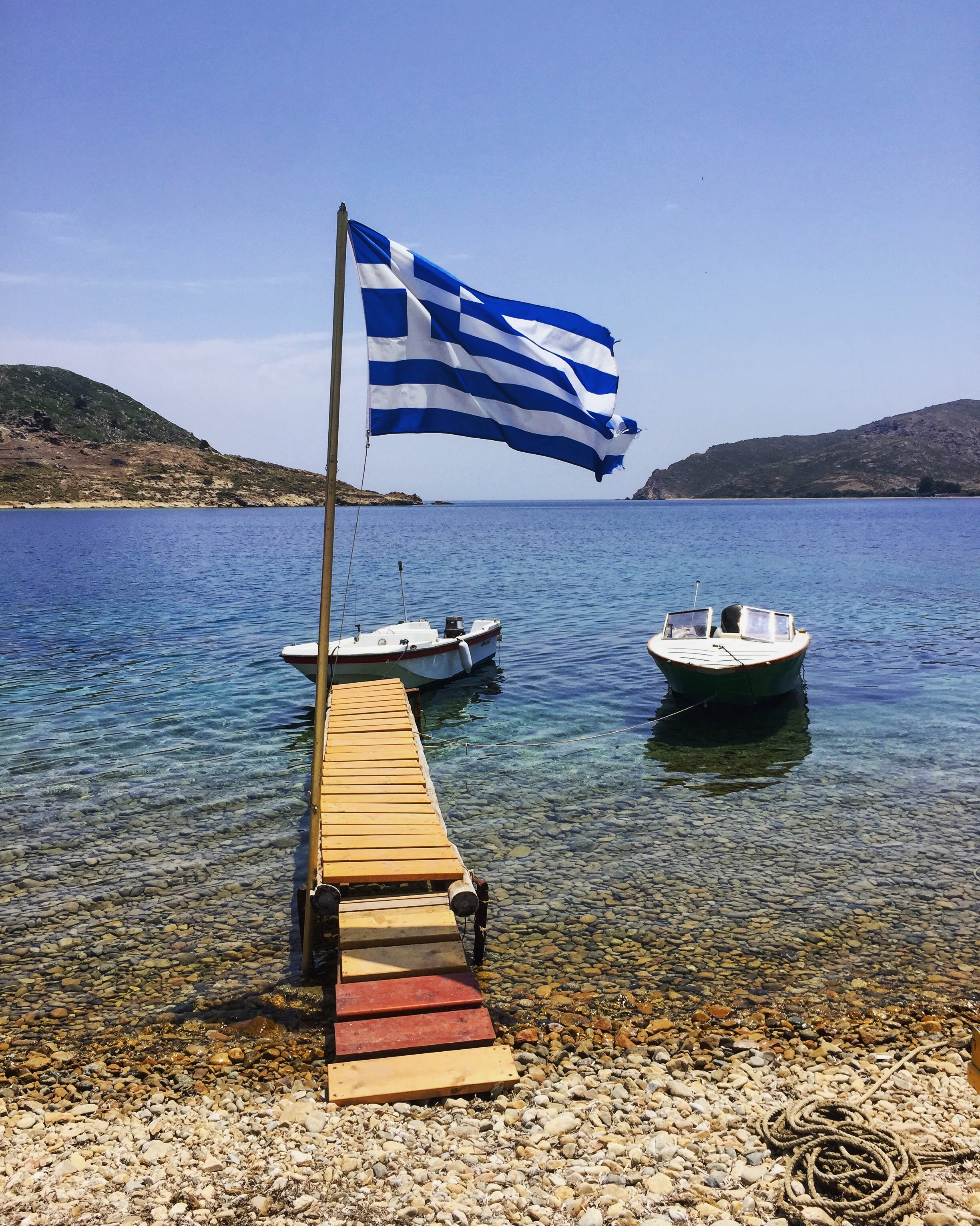 Greek flag and small fishing boats on a clear Aegean bay