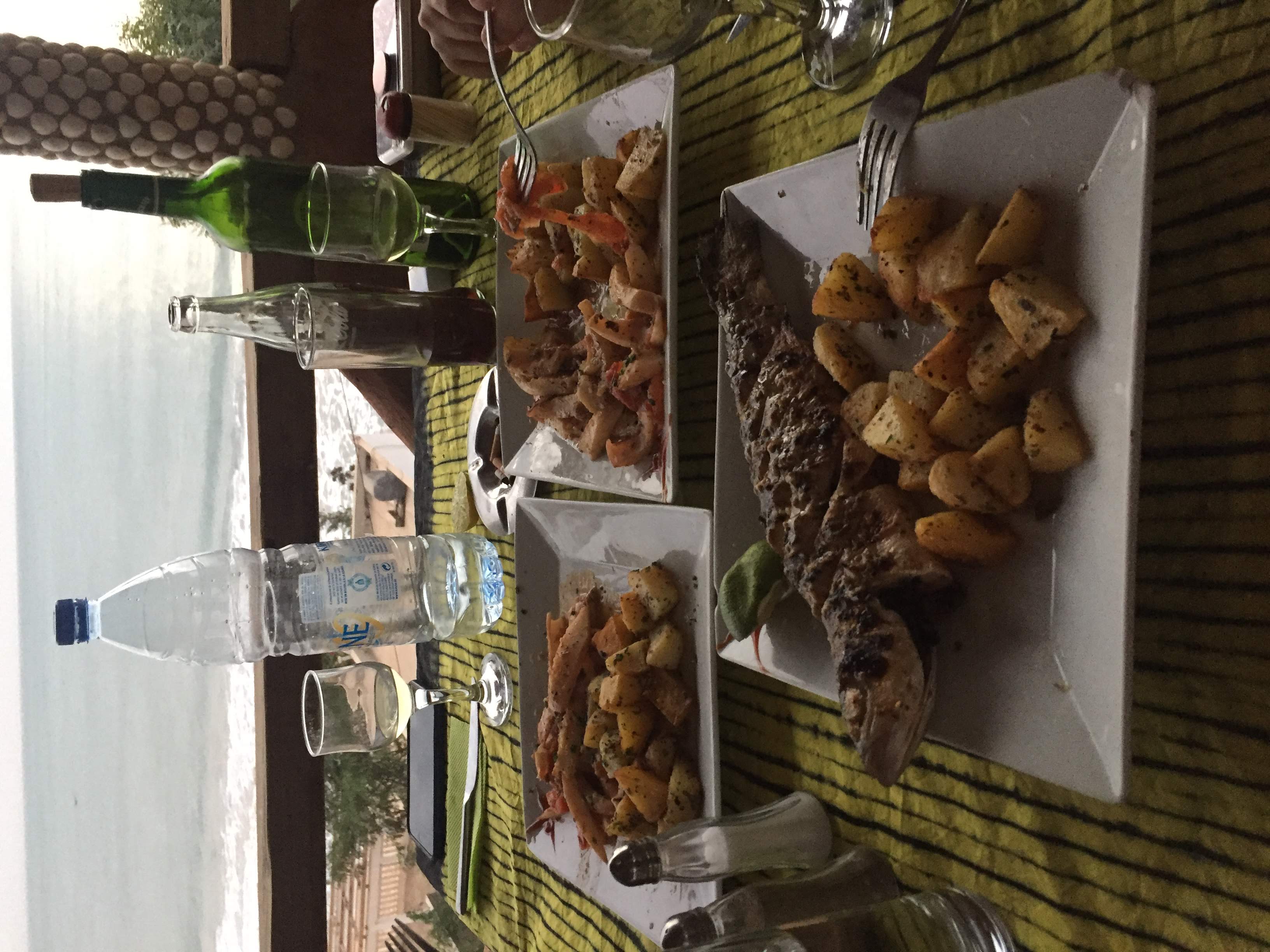 Le Balafon table — grilled whole fish, prawns, roasted potatoes, white wine, Atlantic ocean behind