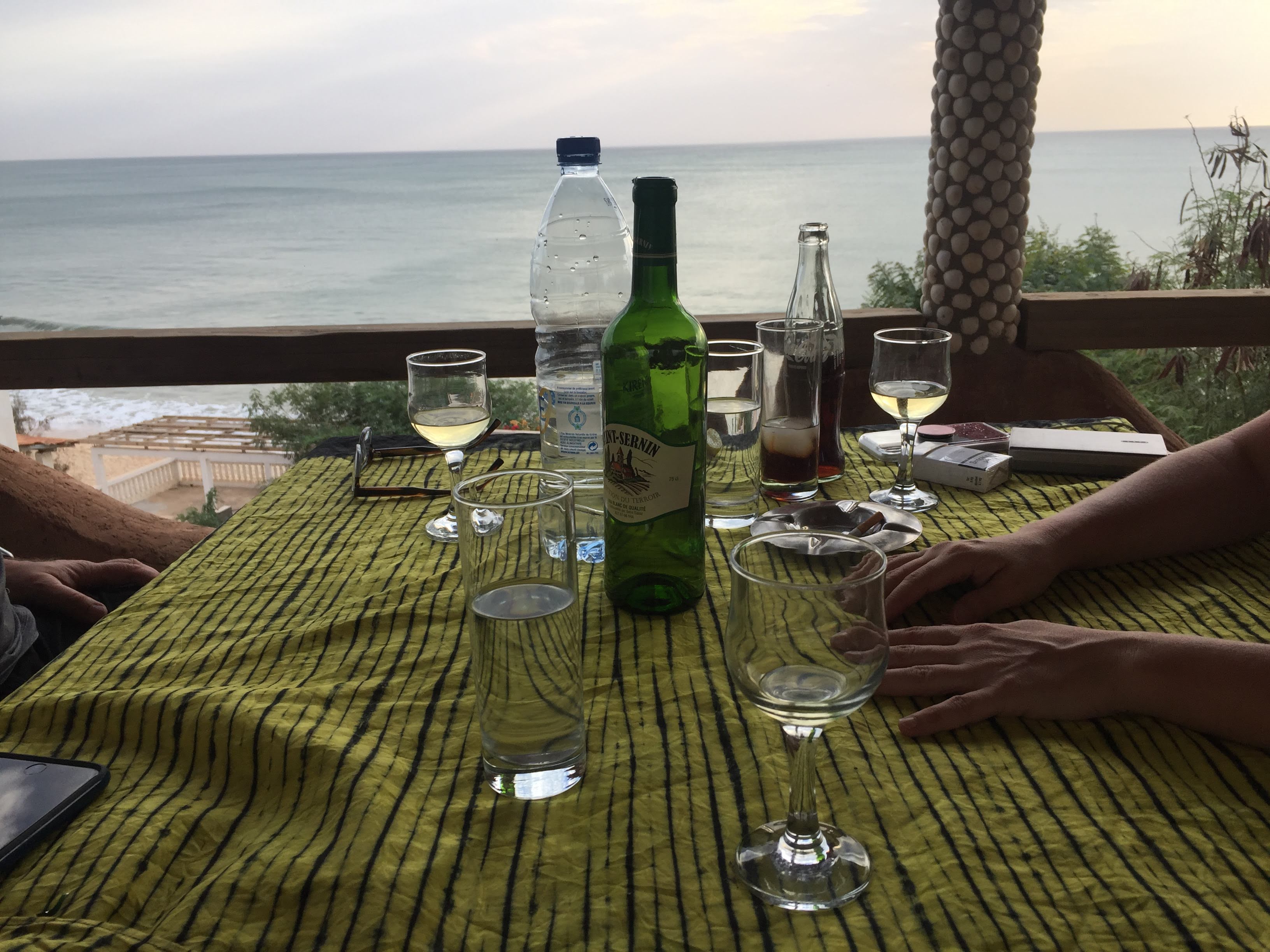 Le Balafon terrace table — wine glasses, white wine bottle, Atlantic ocean behind at dusk