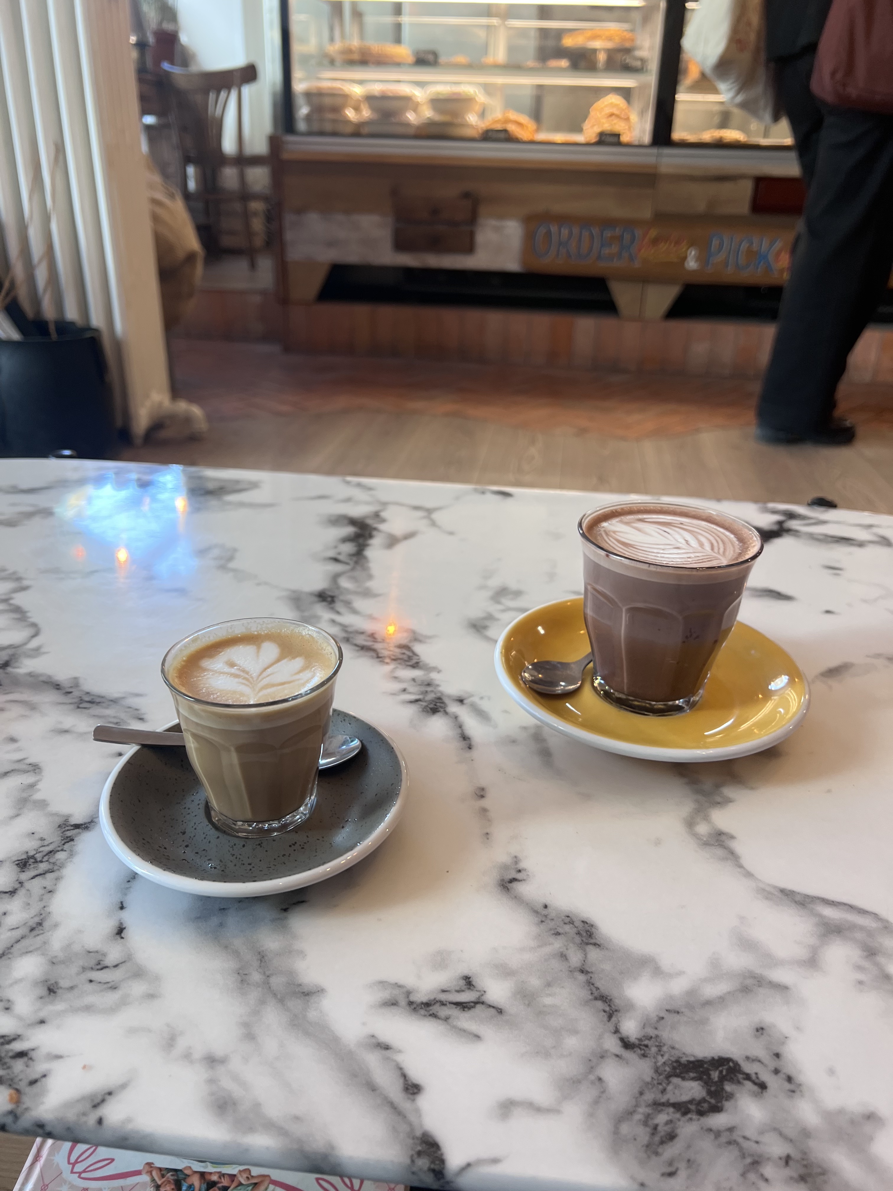 Oh Martine! two drinks on marble table — cortado and hot chocolate, counter behind