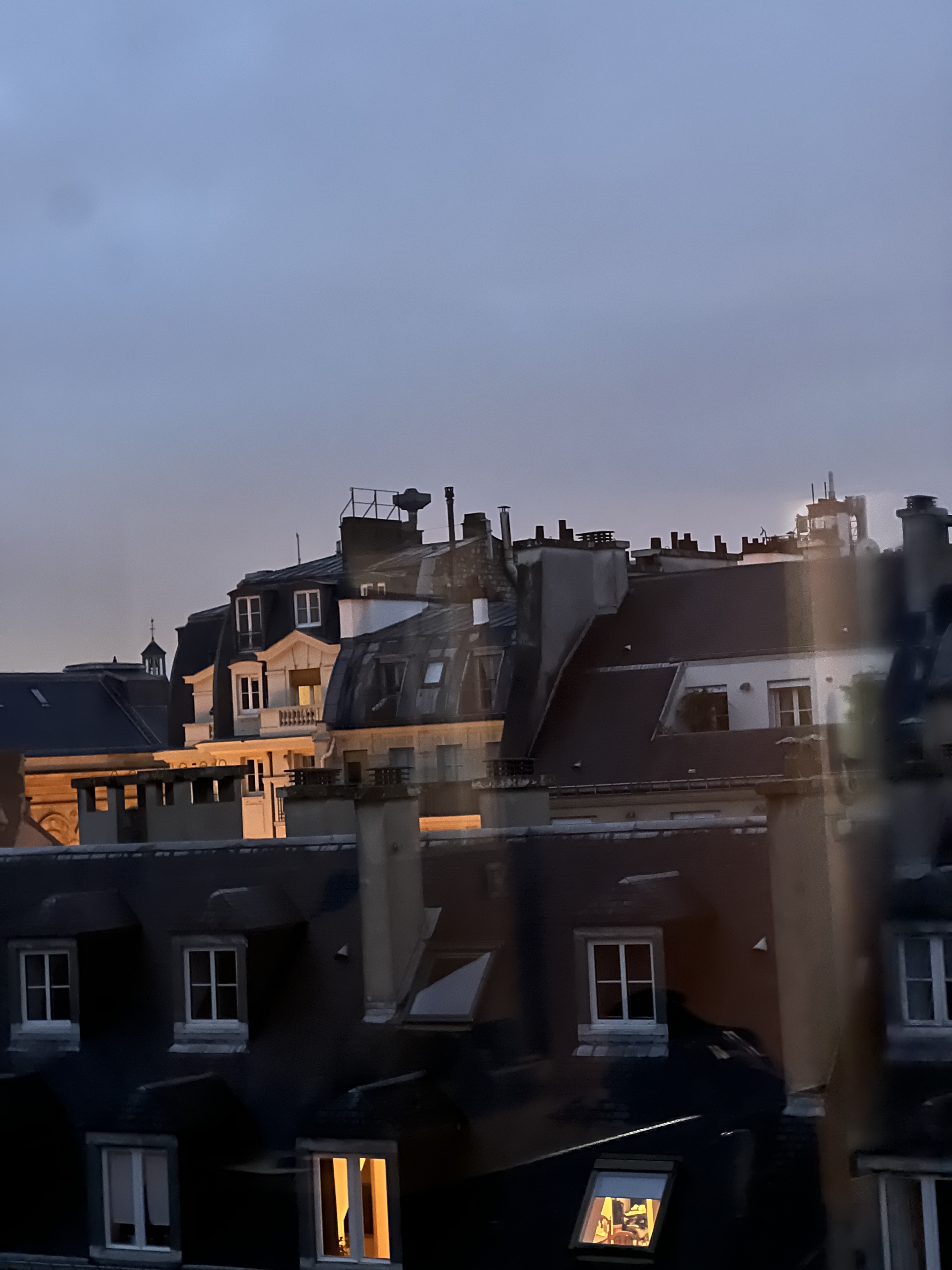 Parisian rooftops at dusk — zinc, lit windows, blue hour