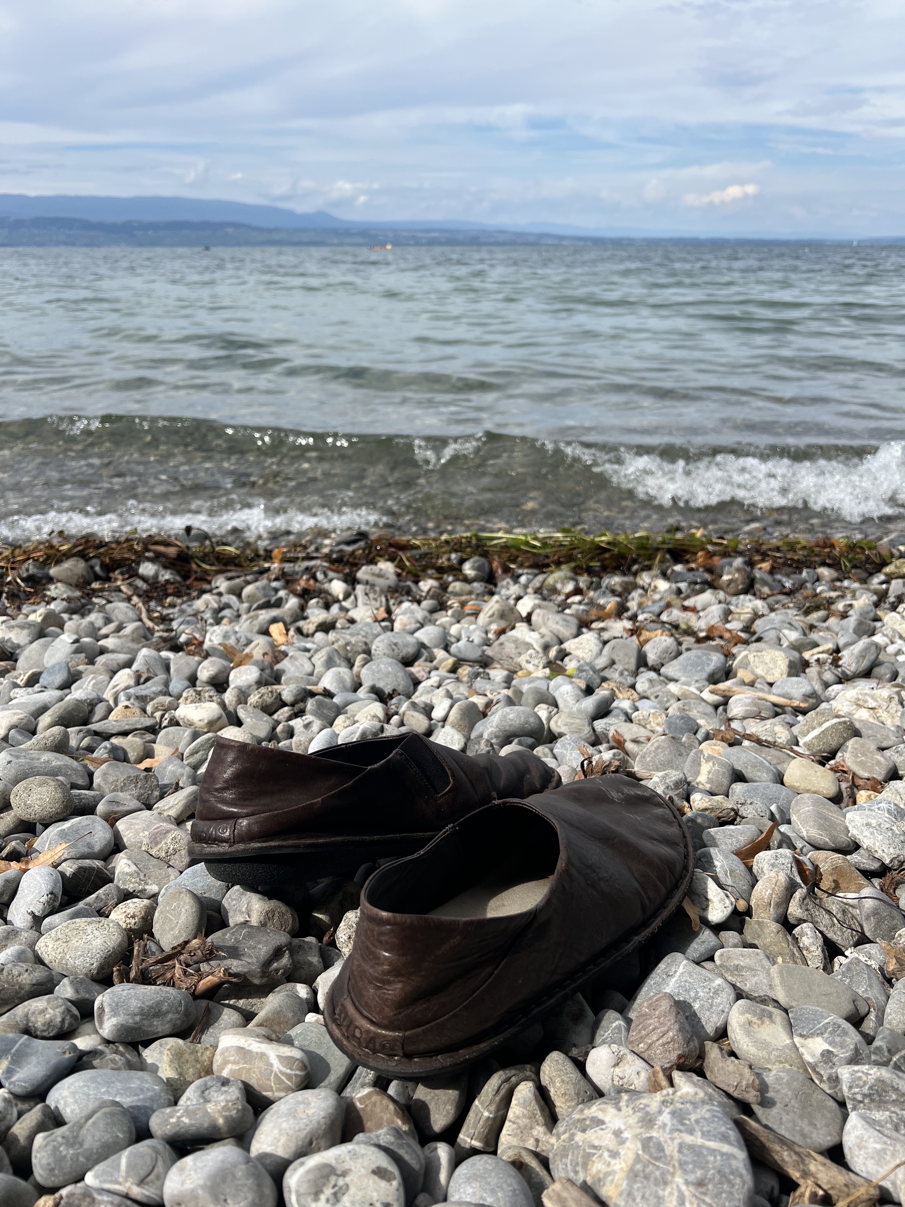 Pebble beach at Sciez-sur-Léman, France — shoes on the stones, lake and Alps in the distance