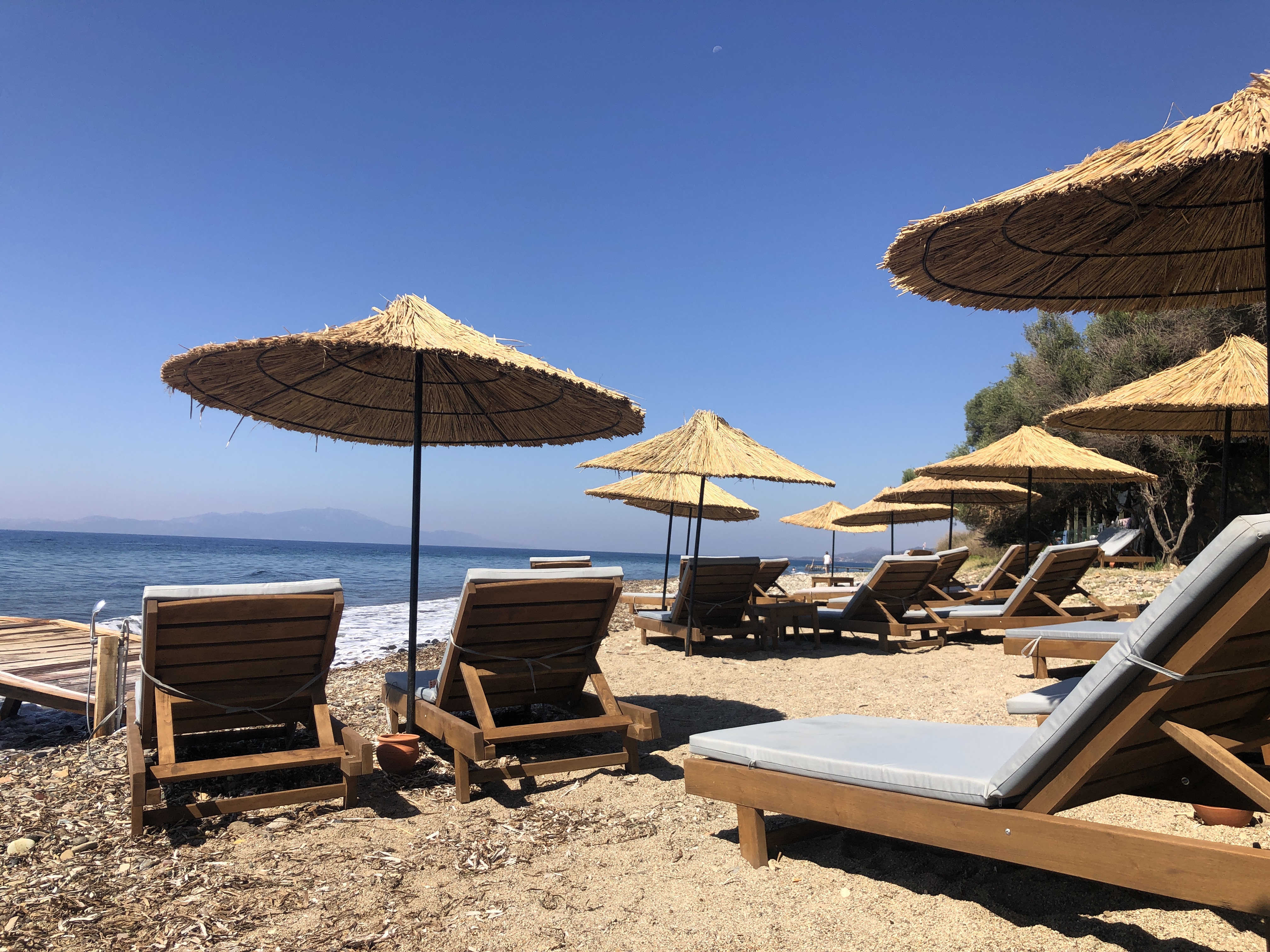 Wooden sun loungers and thatched umbrellas on Simurg Sea's beach, Aegean coast