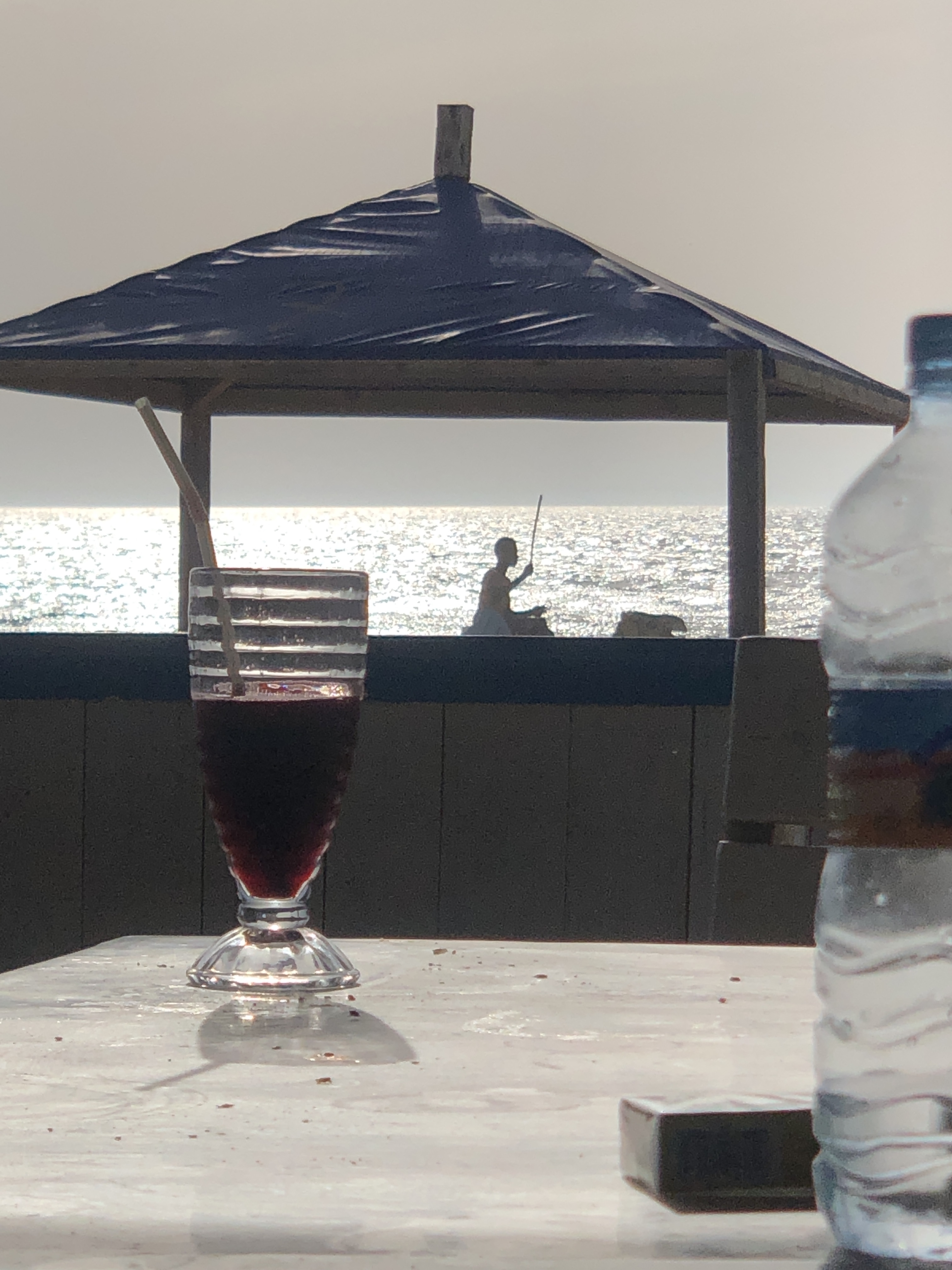 Hibiscus juice at Le Soultane, a fisherman silhouetted against the silver ocean behind