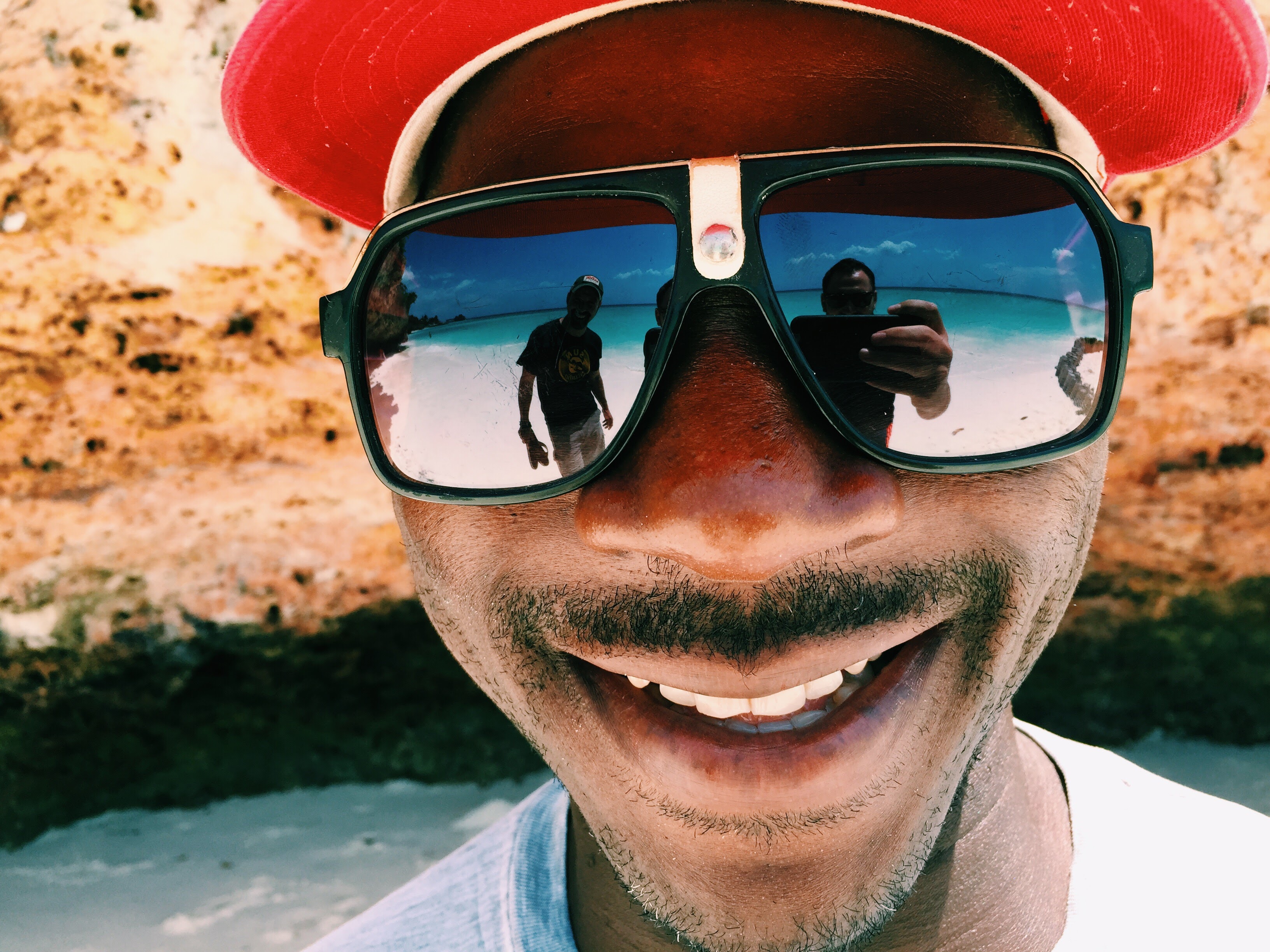 Local with a huge smile and reflective sunglasses, beach and turquoise sea reflected in the lenses