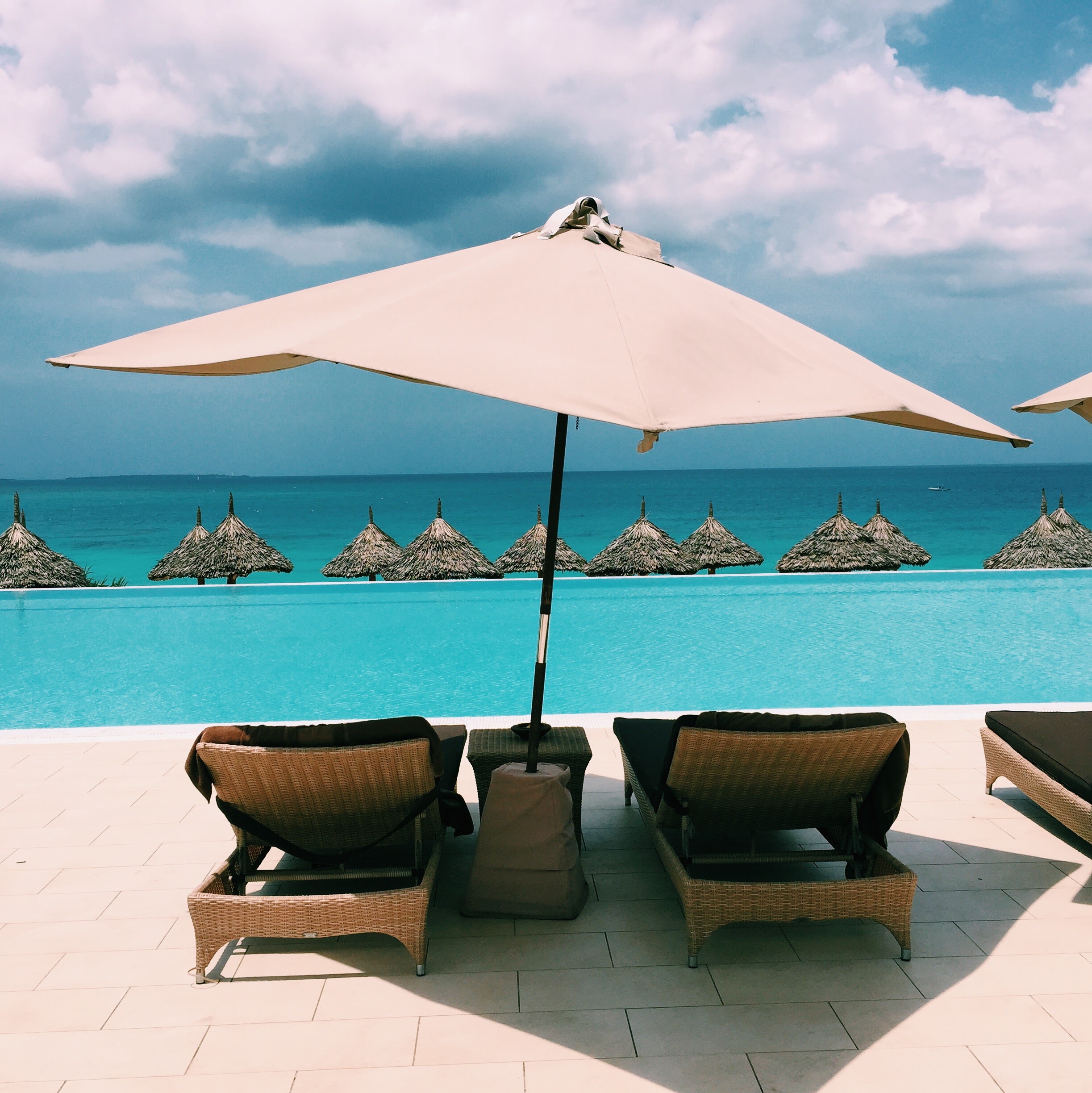 Infinity pool with rattan loungers, thatched beach umbrellas and turquoise Indian Ocean